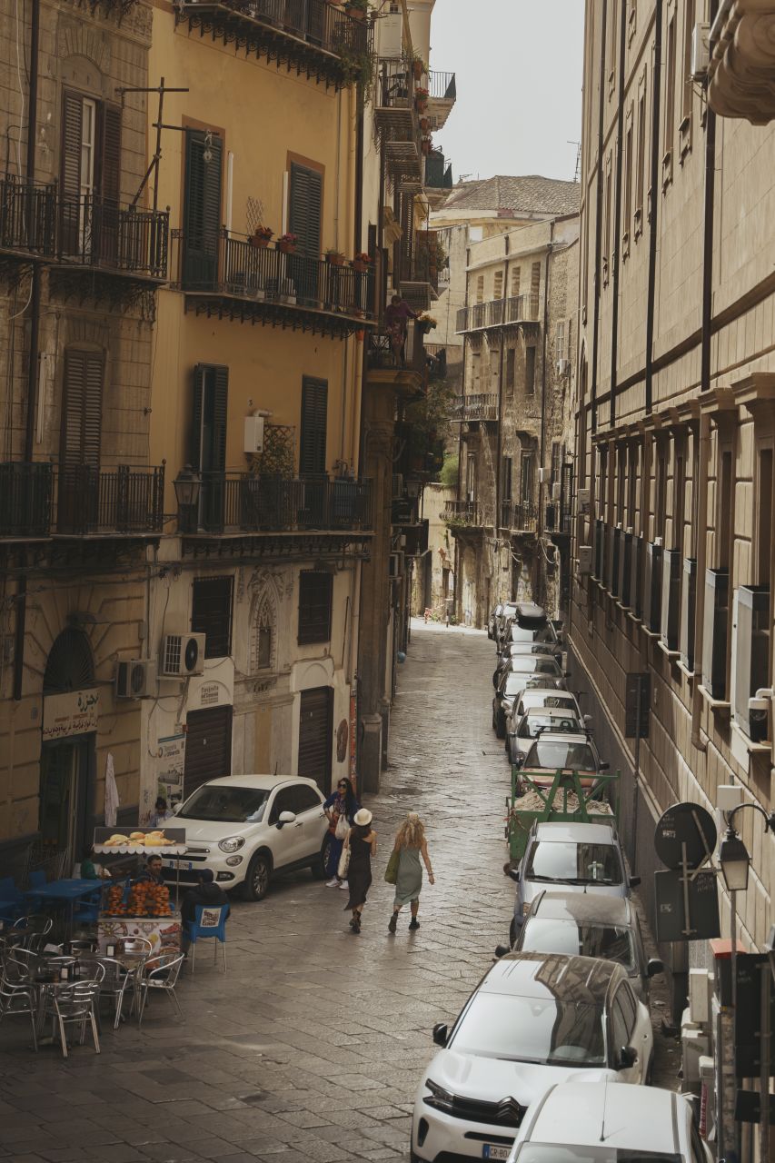 Two women walking in a Palermo street with many parked cars