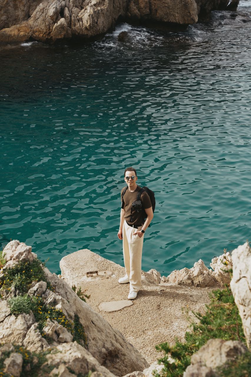 Man standing on a cliff in front of the ocean at Punta Sant'Elia