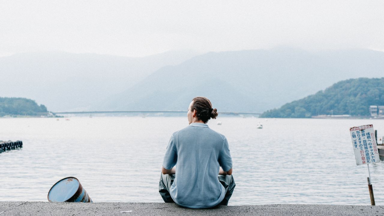 A man in a blue shirt sitting and watching Kawaguchiko Lake, Japan.