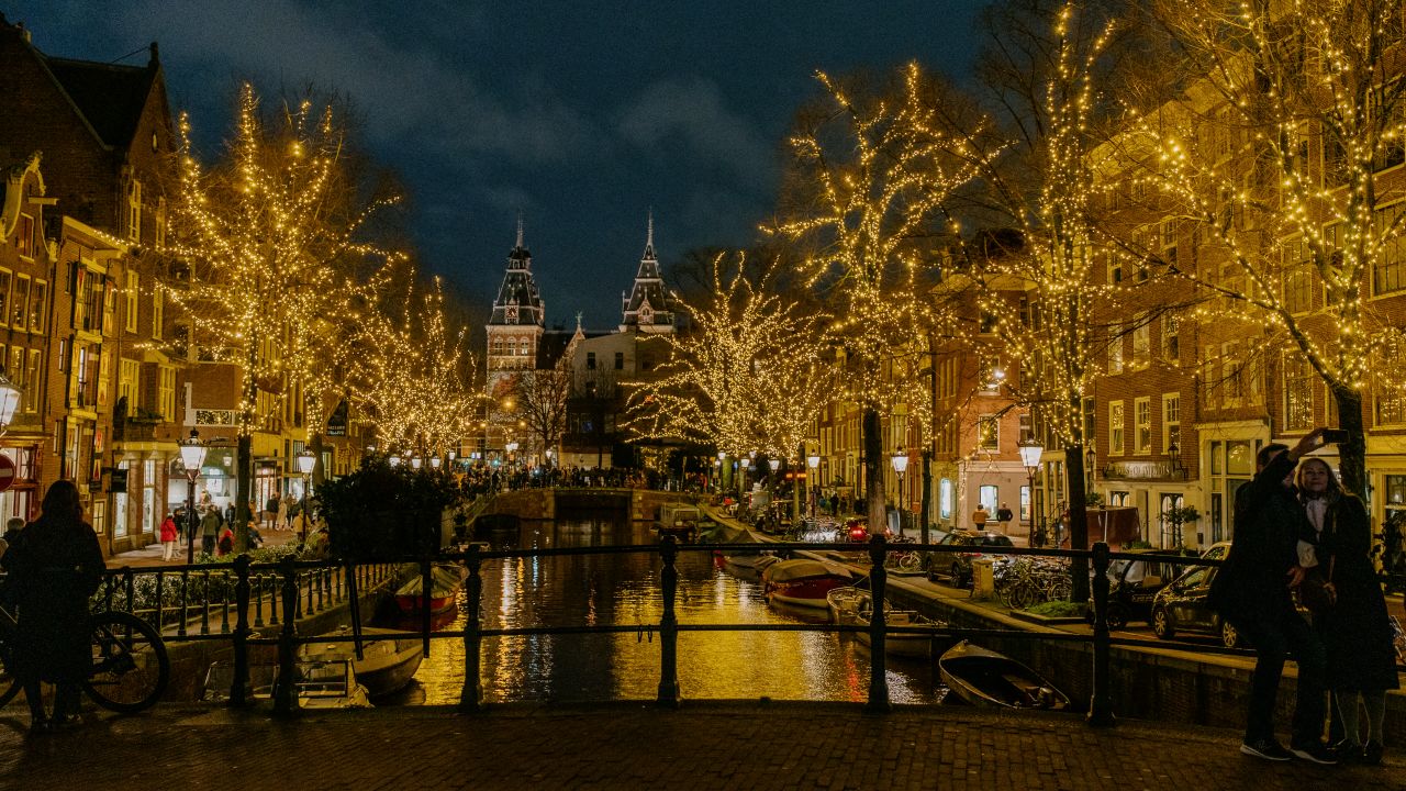 Christmas light-decorated trees near a canal in Amsterdam.